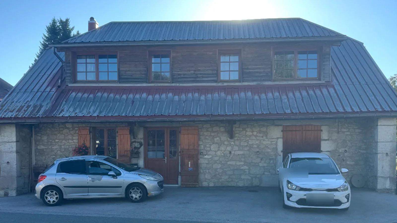 Maison en pierre dont le toit en bac acier est terni et décoloré.